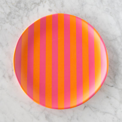 A round Stripe Melamine Plate with alternating vertical pink and orange stripes on a marble table.
