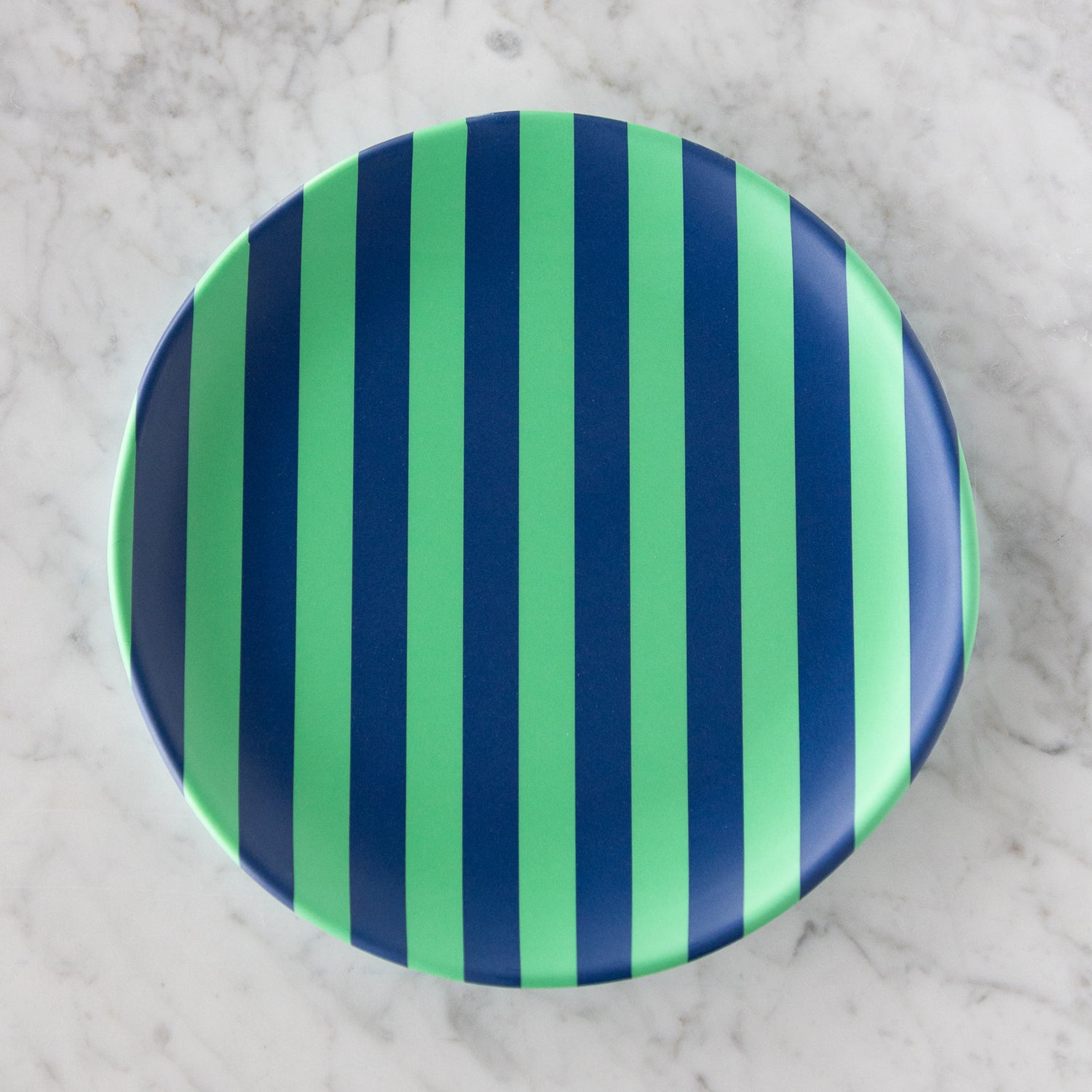A round Stripe Melamine Plate with alternating vertical mint and navy stripes on a marble table.