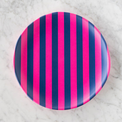 A round Stripe Melamine Plate with alternating vertical hot pink and navy stripes on a marble table.