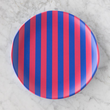 A round Stripe Melamine Plate with alternating vertical pink and blue stripes on a marble table.