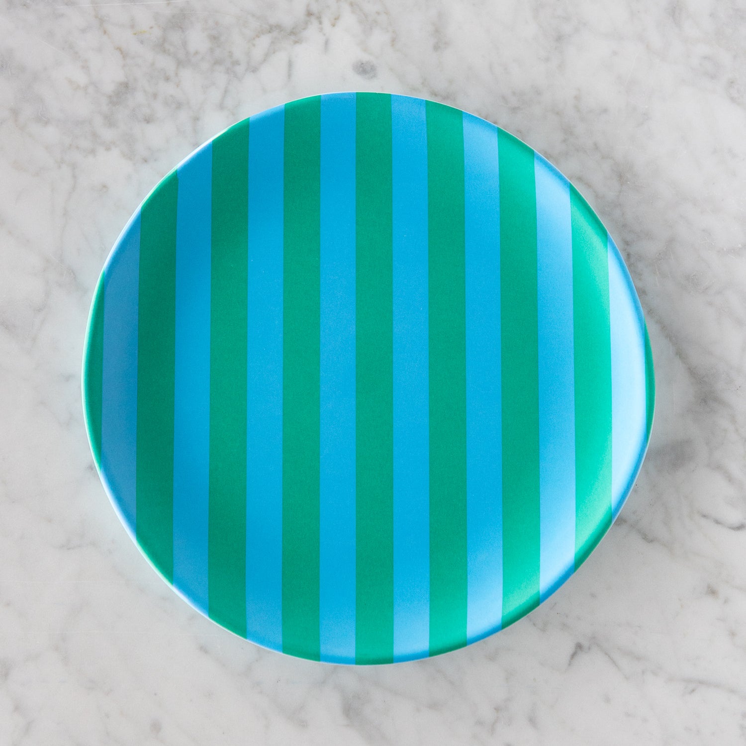 A round Stripe Melamine Plate with alternating vertical light blue and turquoise stripes on a marble table.