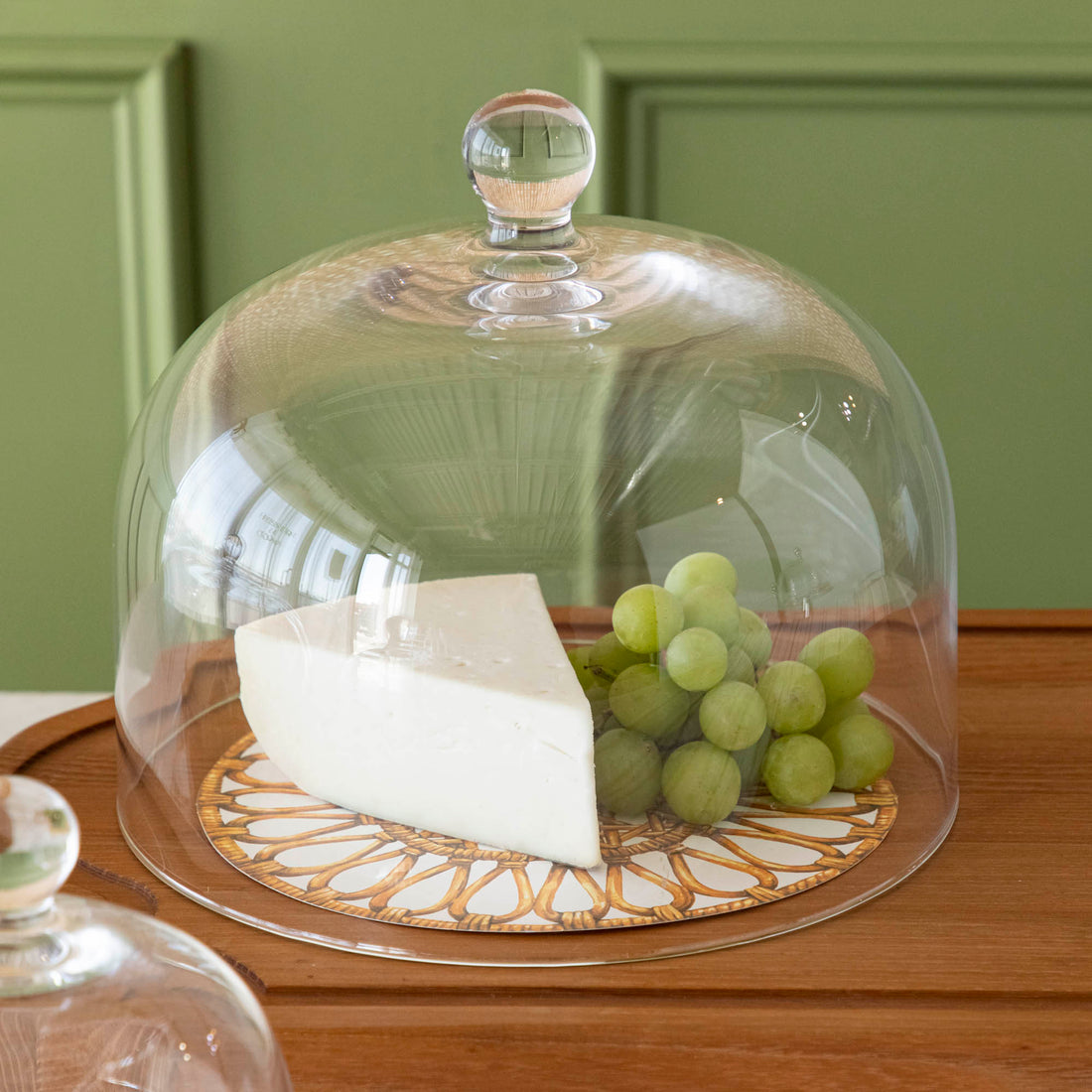 Various cheeses and grapes displayed under a Casafina Living glass dome serveware on a kitchen counter.