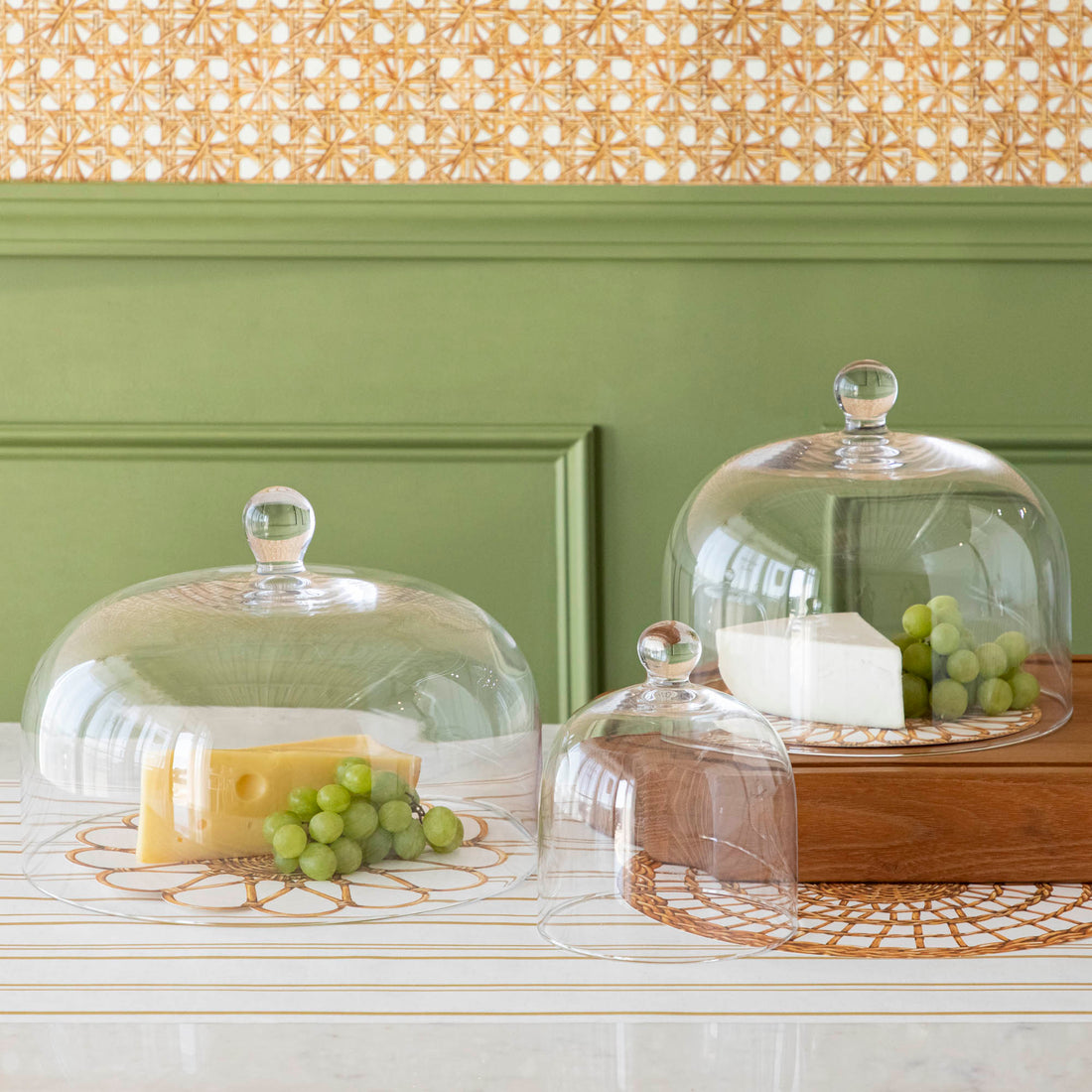 Various cheeses and grapes displayed under a Casafina Living glass dome serveware on a kitchen counter.