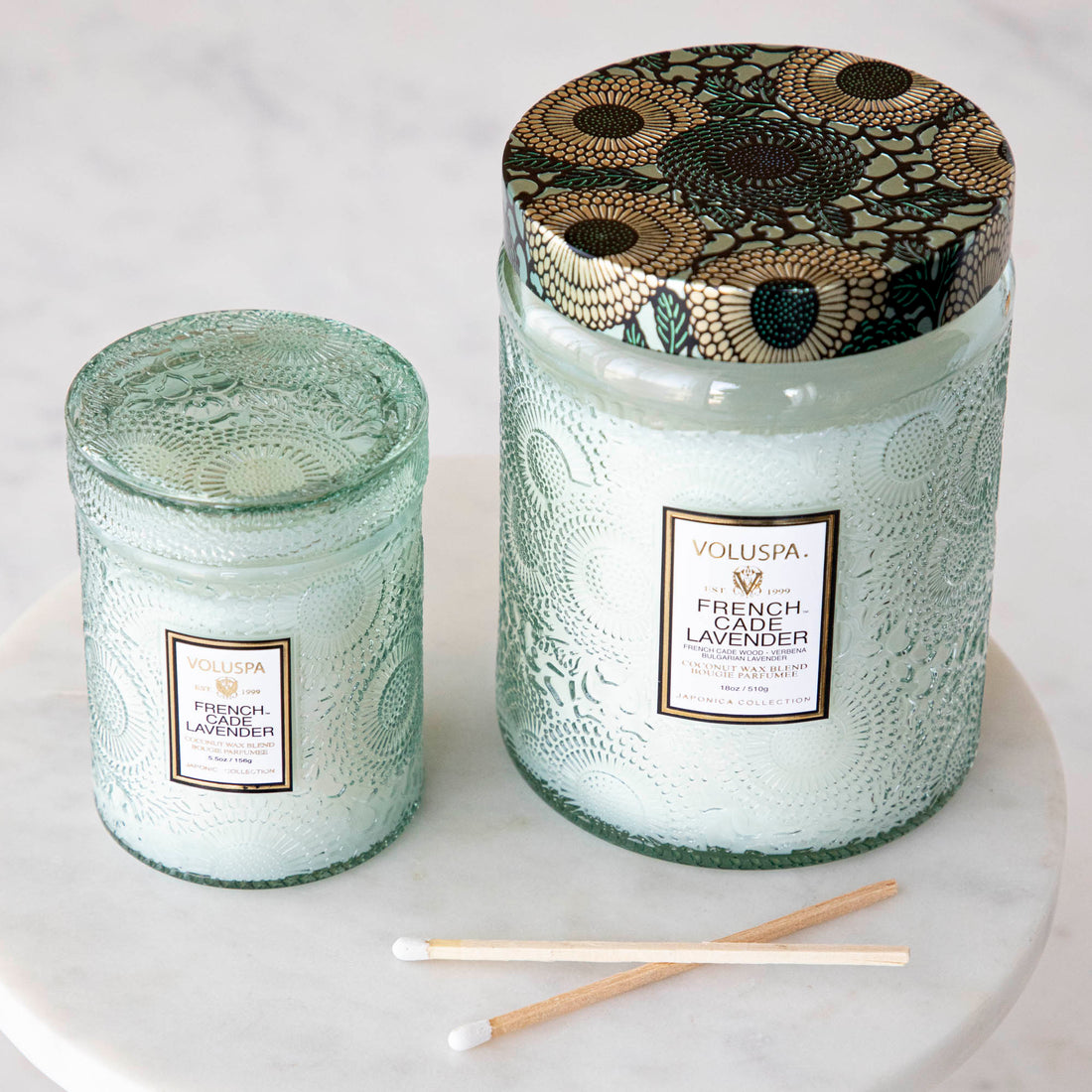 Two Voluspa French Cade Lavender candles on a marble surface with lemon verbena matchsticks.