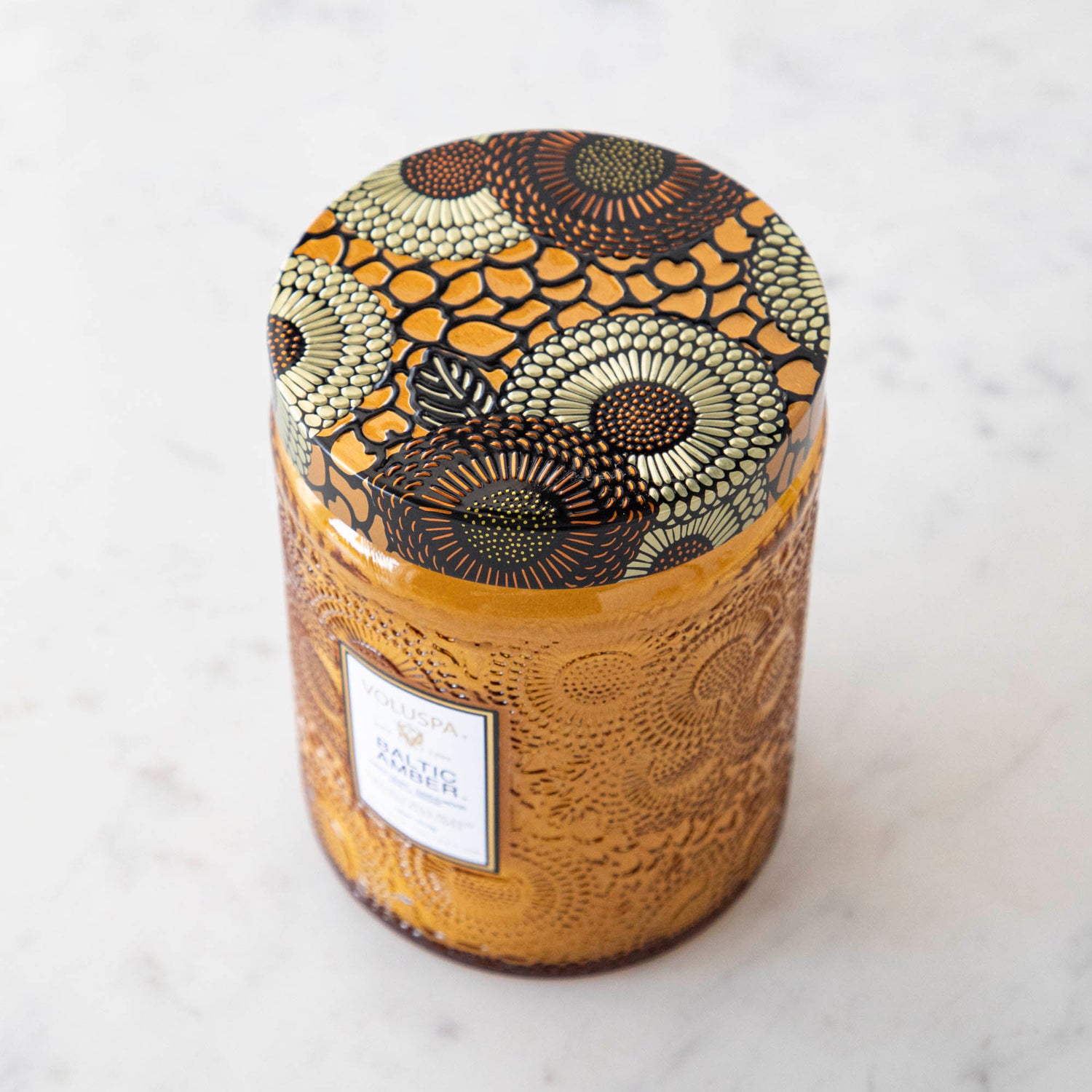 Two Voluspa Baltic Amber candles with matches on a marble surface.