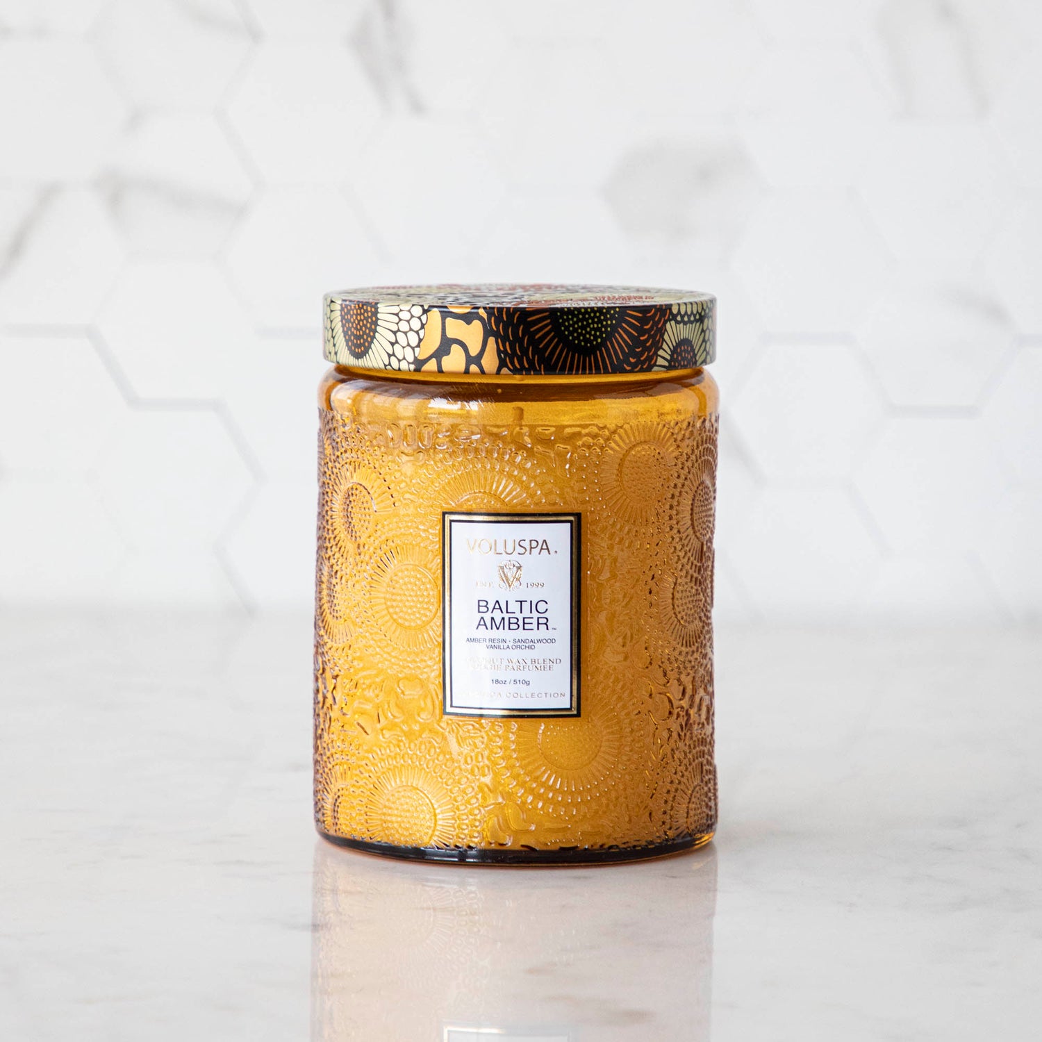 Two Voluspa Baltic Amber candles with matches on a marble surface.