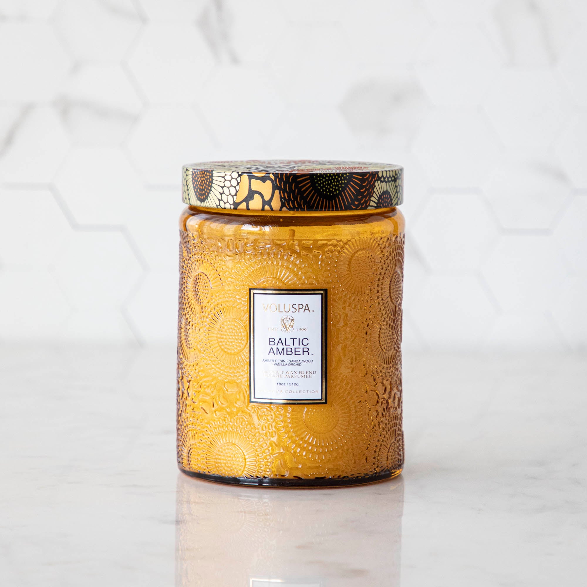 Two Voluspa Baltic Amber candles with matches on a marble surface.