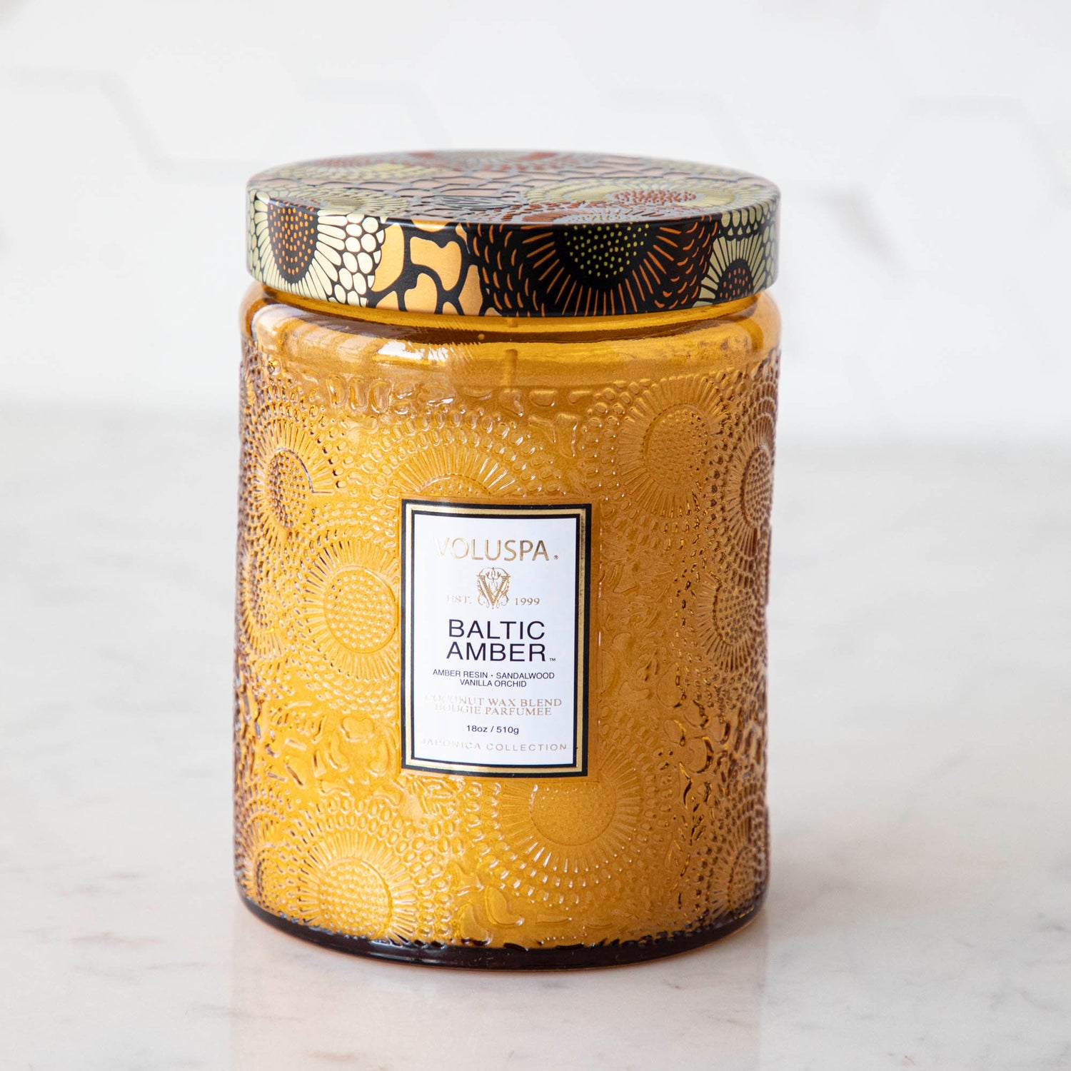 Two Voluspa Baltic Amber candles with matches on a marble surface.