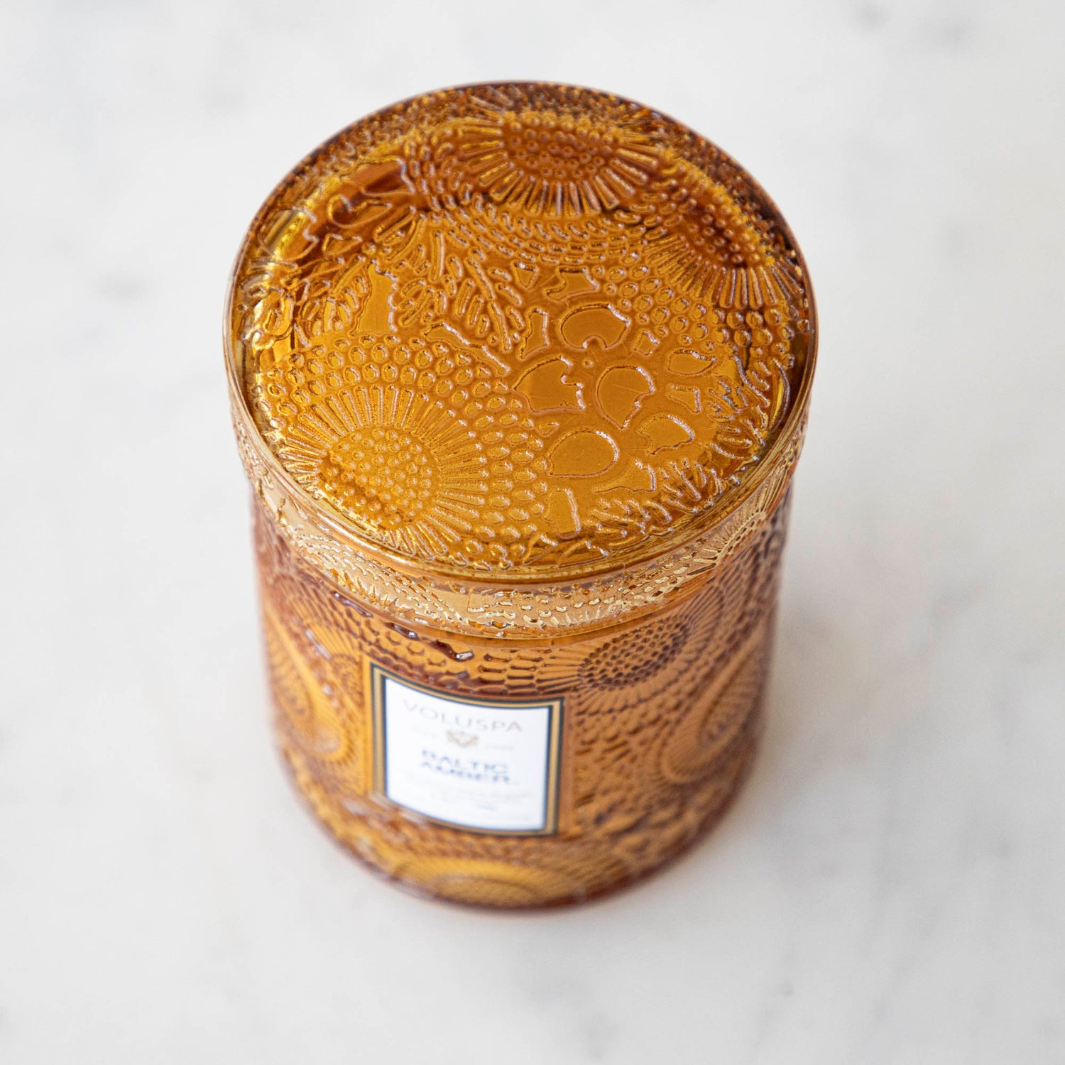 Two Voluspa Baltic Amber candles with matches on a marble surface.