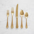 A set of Mepra Dolce Vita Pewter Oro 5-Piece Place Setting flatware, including two forks, a knife, and two spoons, neatly arranged on a marble surface.