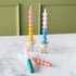 Four Colorful Bubble Taper Candles in pastel hues, two upright in sprinkle-filled glass holders and two lying on a white marble surface.