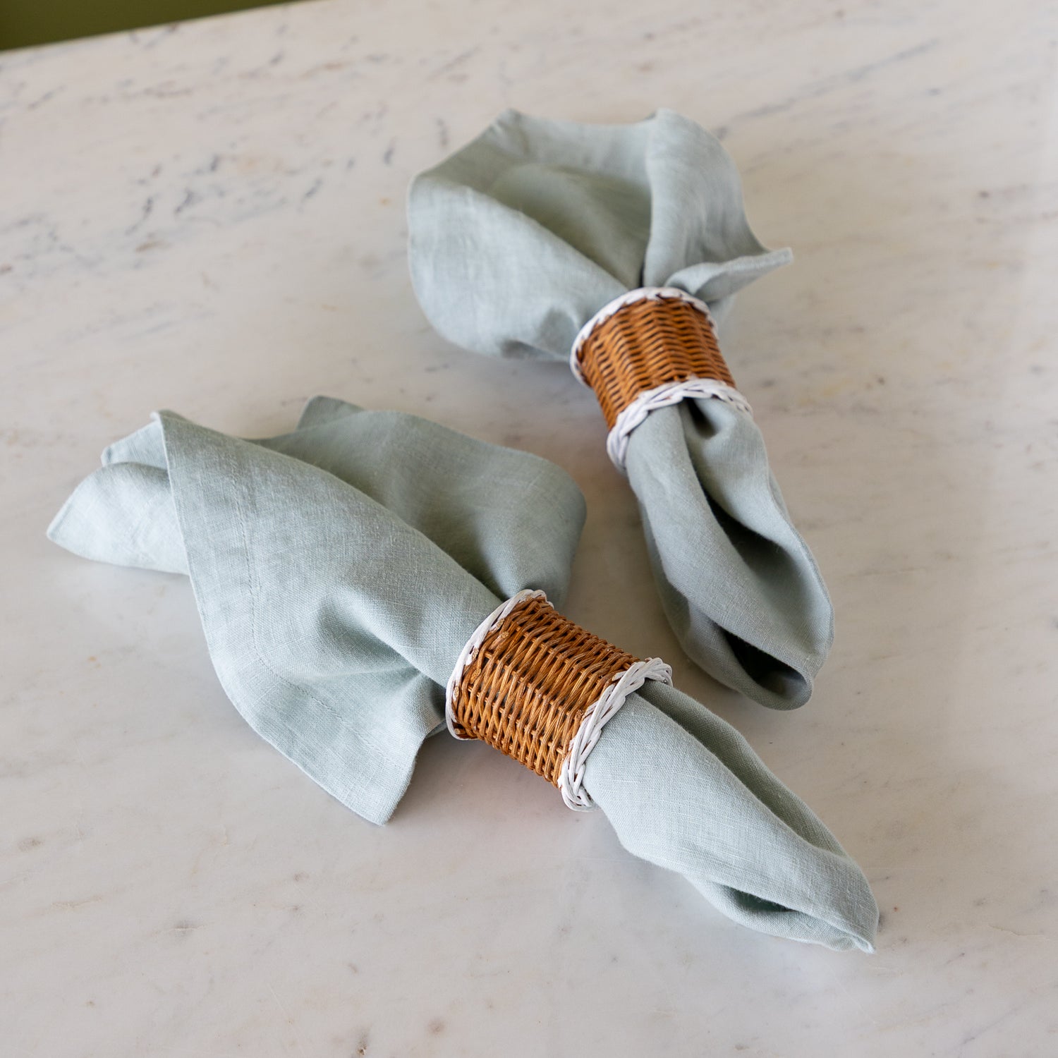 Two, Two-Tone Rattan Napkin Rings holding elegant bluish-gray cloth napkins.