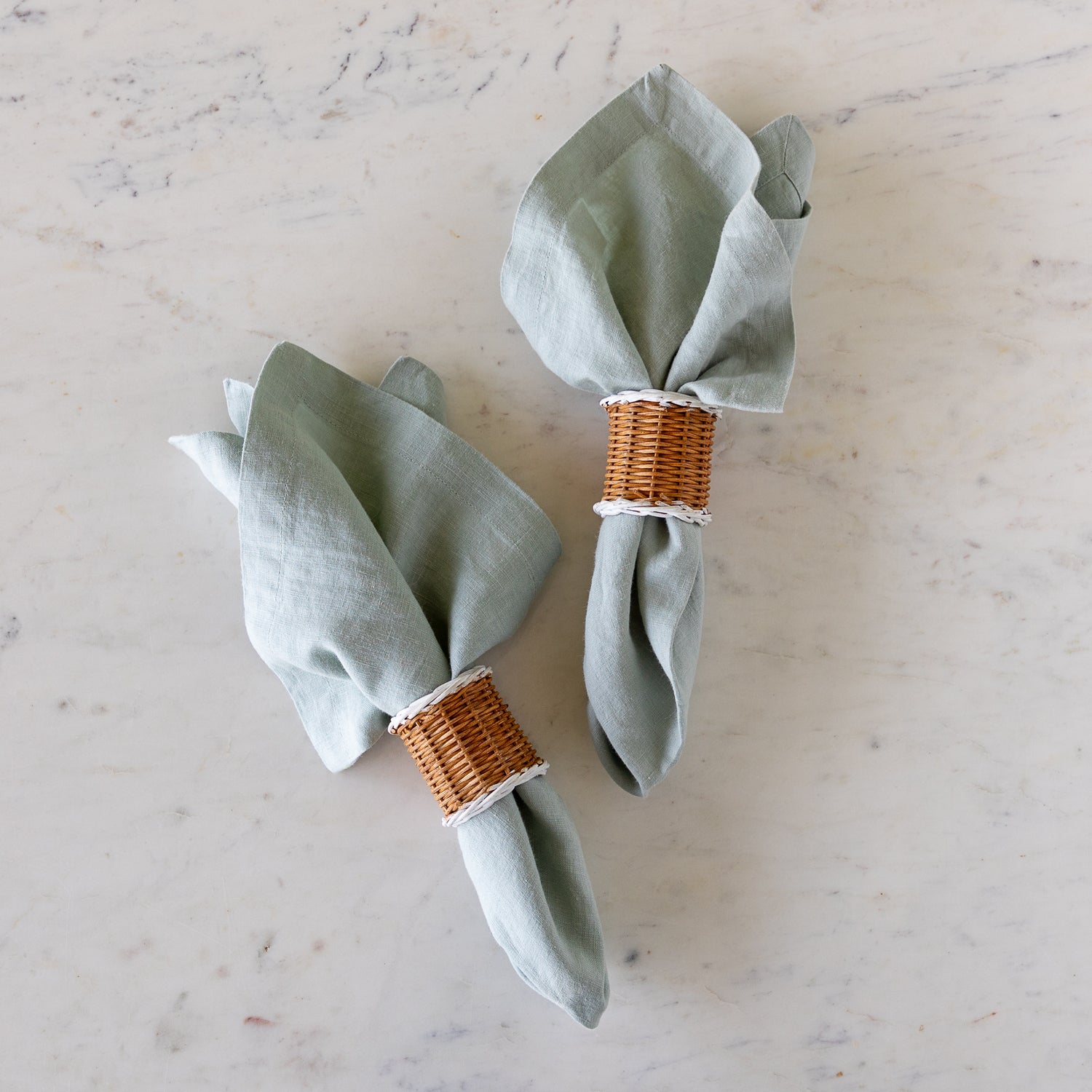 Two, Two-Tone Rattan Napkin Rings holding elegant bluish-gray cloth napkins.