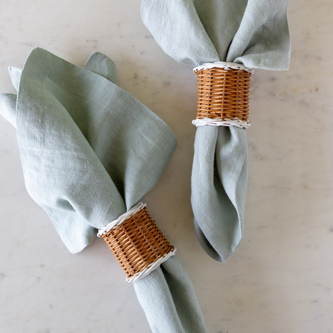 Two, Two-Tone Rattan Napkin Rings holding elegant bluish-gray cloth napkins.
