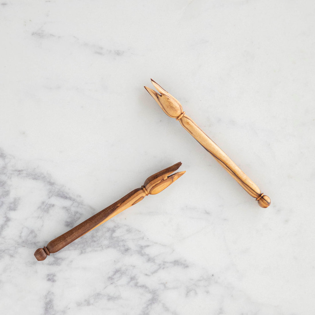 Two wooden spoons and a Natural Olivewood Olive Wood Picker on a marble surface.