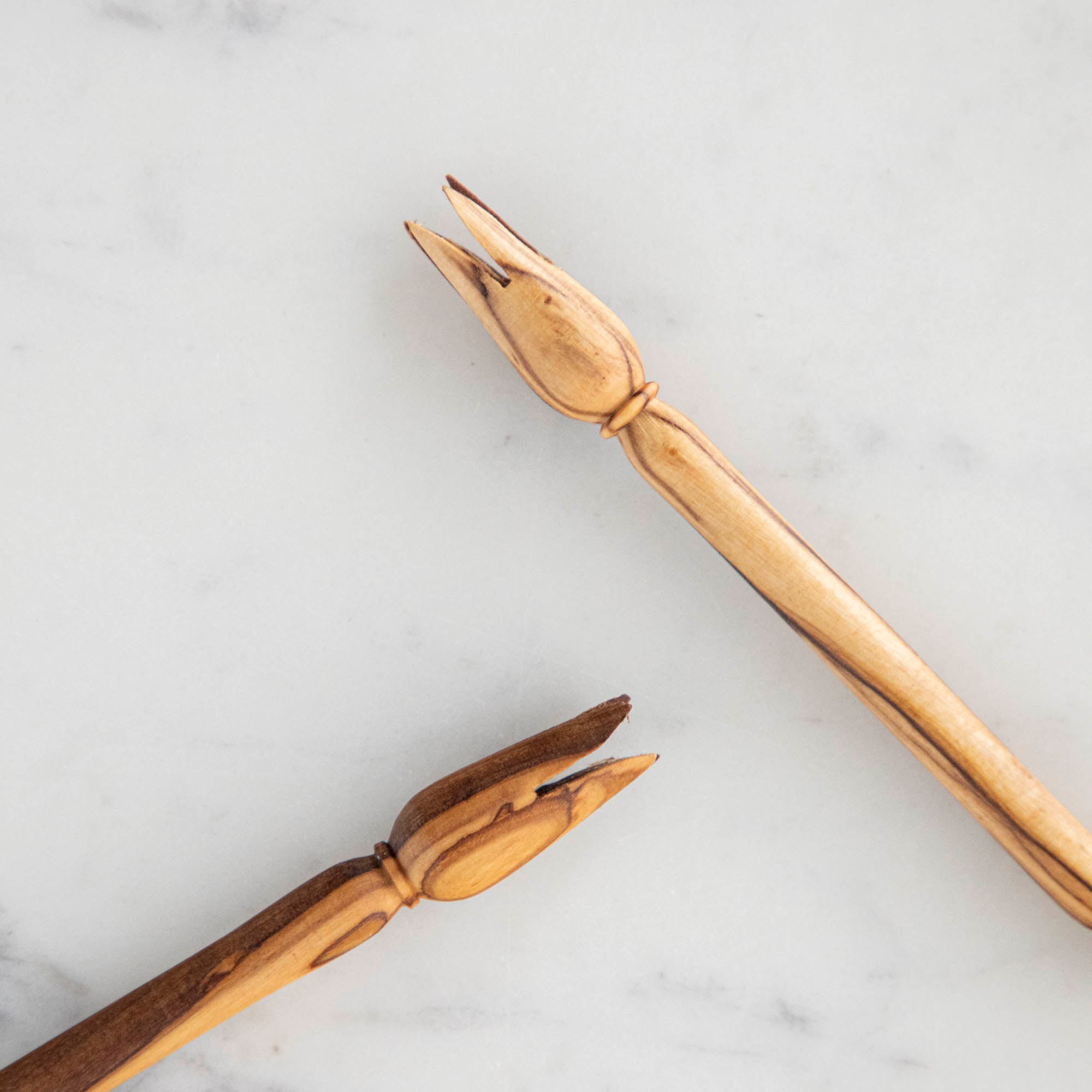 Two wooden spoons and a Natural Olivewood Olive Wood Picker on a marble surface.