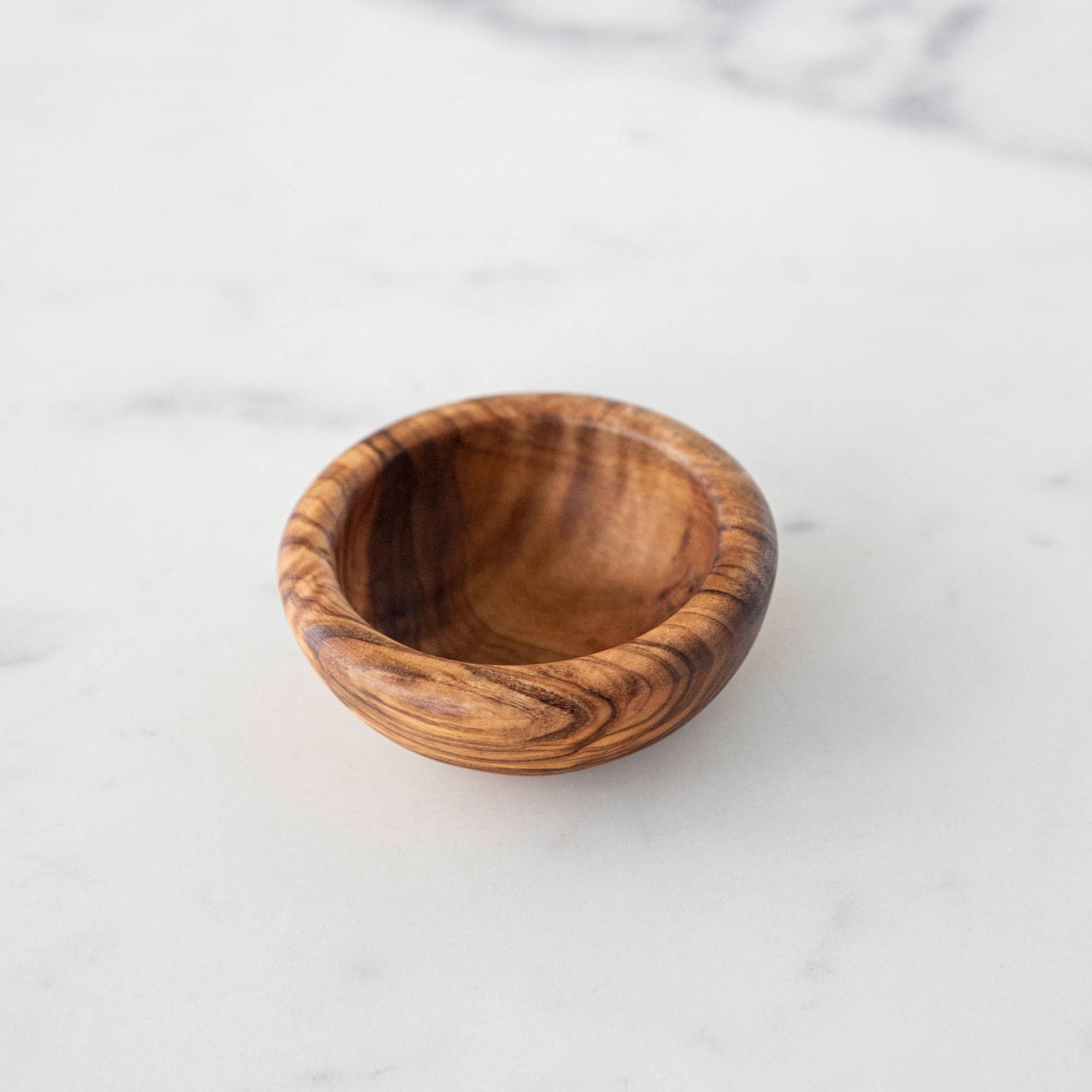 Three Natural Olivewood Pinch Bowls with salt and a sprig of rosemary on a kitchen counter.