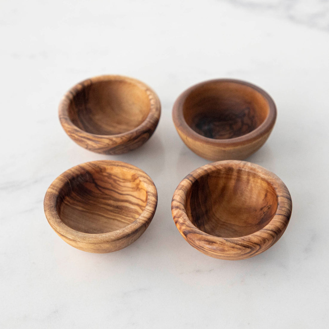 Three Natural Olivewood Pinch Bowls with salt and a sprig of rosemary on a kitchen counter.
