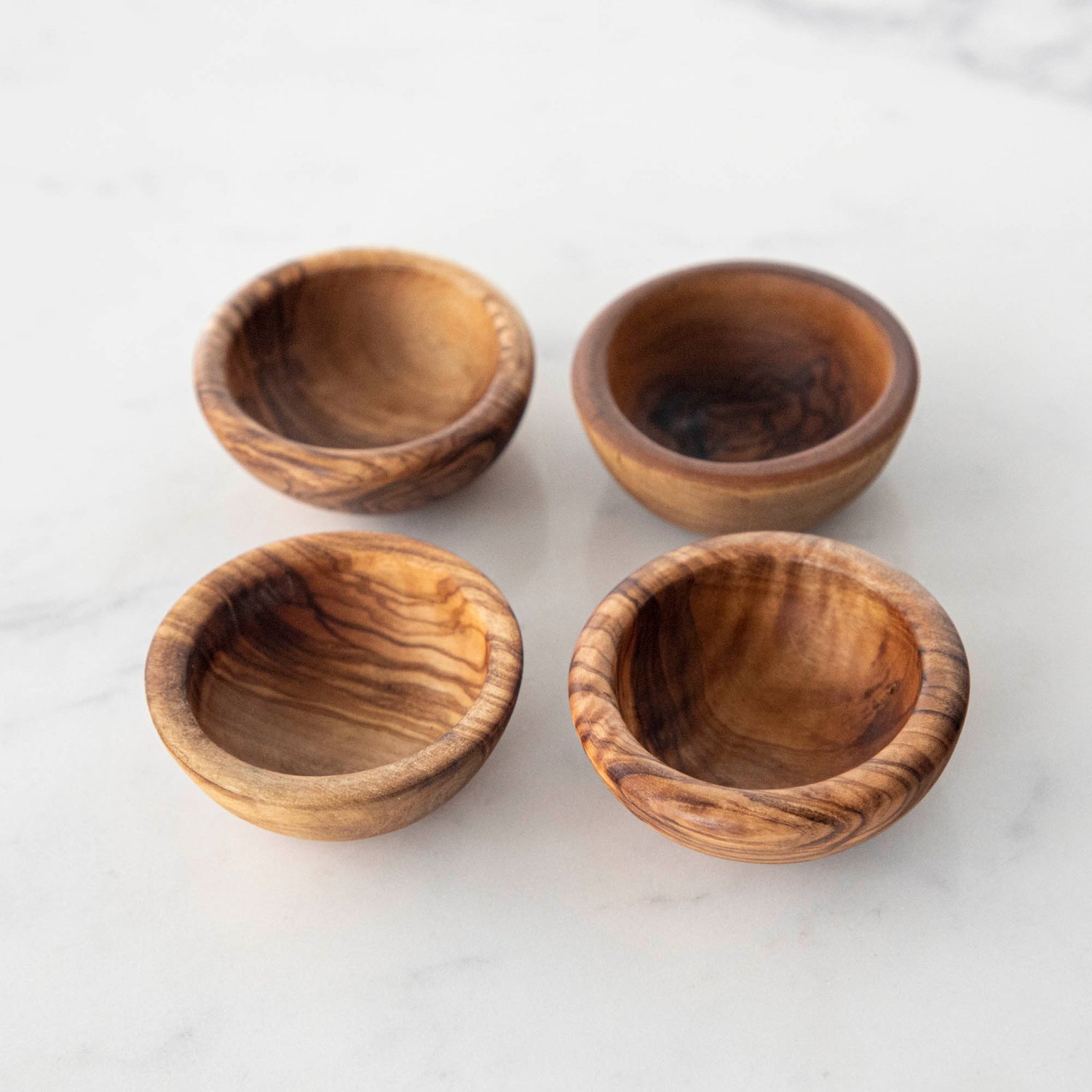 Three Natural Olivewood Pinch Bowls with salt and a sprig of rosemary on a kitchen counter.