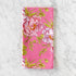 A pink cotton napkin, made in India, features a colorful illustration of pink flowers and green leaves and is displayed on a marble table.