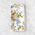 A white cotton napkin, made in India, features a colorful illustration of flowers and leaves and is displayed on a marble table.