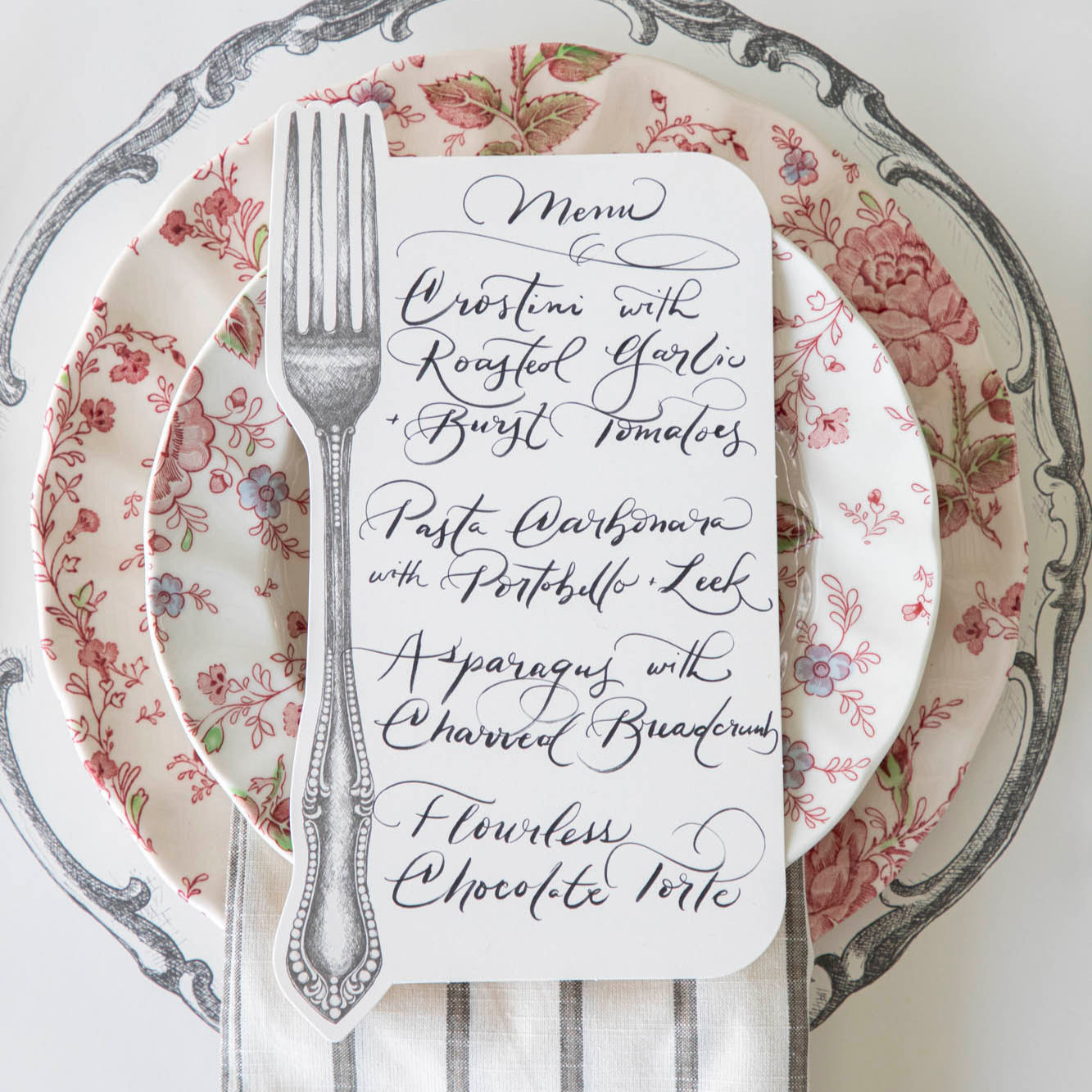 Vintage Fork Table Card with a menu written on it, resting on dinner plates on a table setting for one.