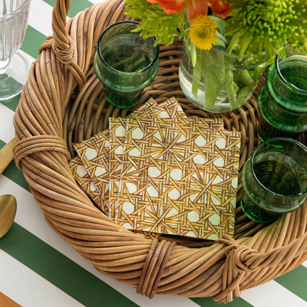 A stack of Rattan Weave Cocktail Napkins on a beverage tray with glasses and a vase of flowers.