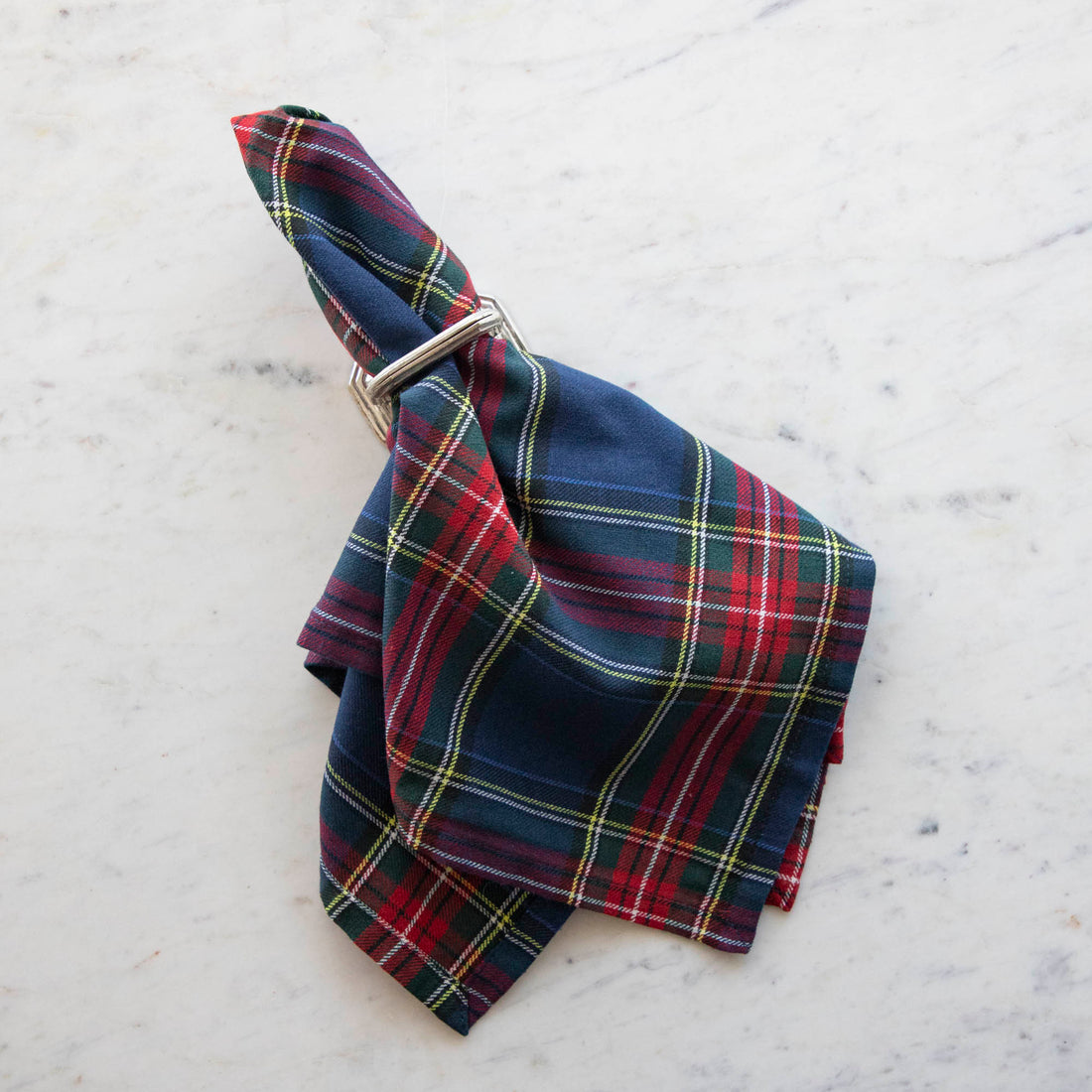 A plaid necktie with a windsor knot on a 100% cotton Taylor Linen Cape Breton napkin on a marble surface.