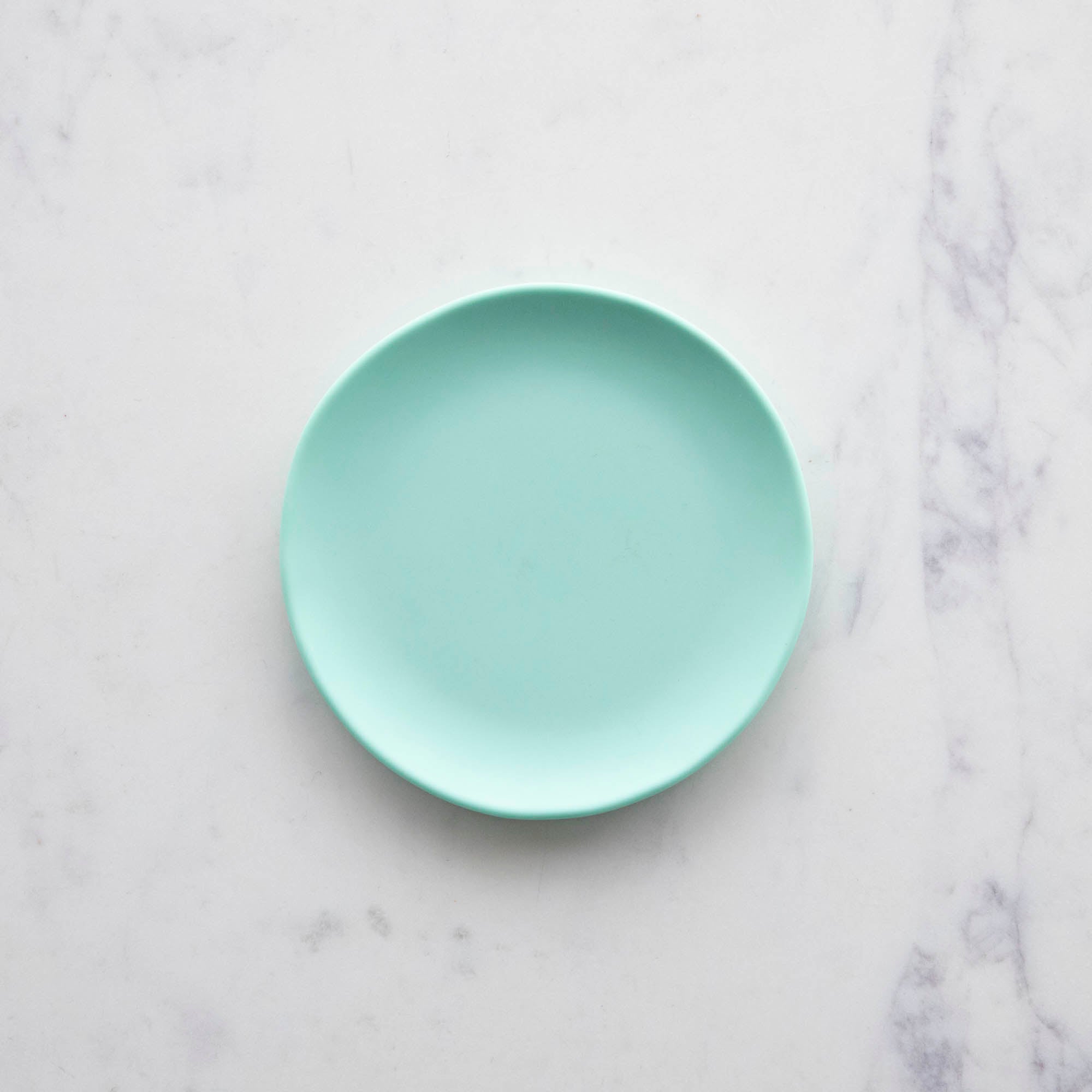 A 6&quot; mint Rainbow Melamine Plate by Glitterville on a marble surface.