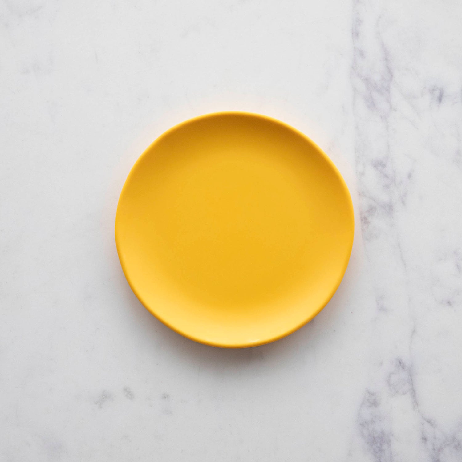 A Glitterville 6&quot; Rainbow Melamine Plate on a marble surface.