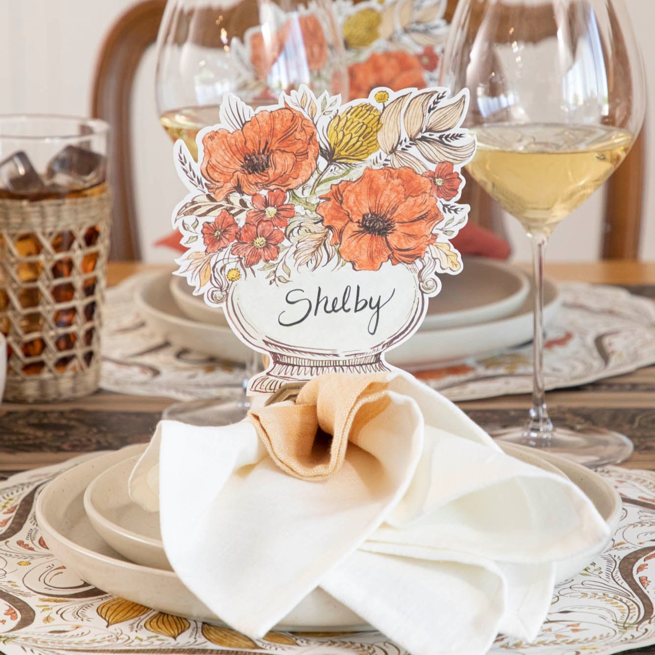 The Autumn Arrangement Place Card with the name &quot;Shelby&quot; written on it, on an elegant fall themed table setting.