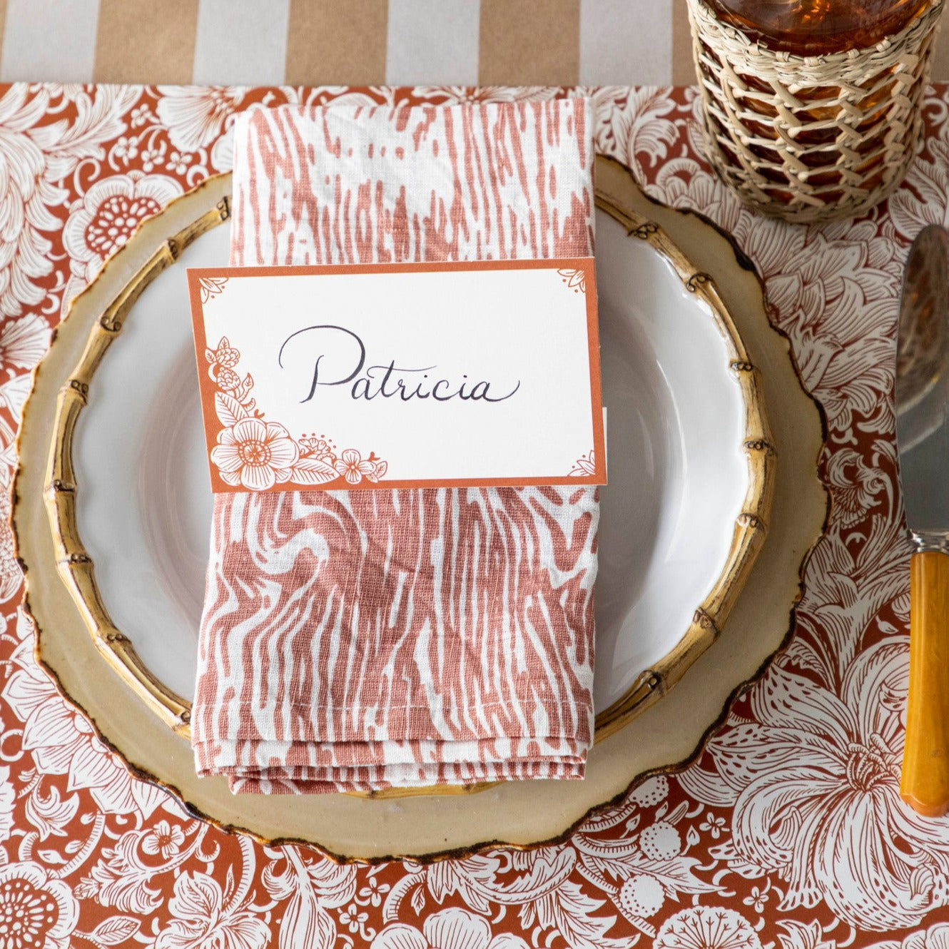 A free-standing, rectangular white table card with a dark orange frame around the edges, embellished with dark orange linework flower designs in the corners.