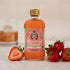A bottle of Hester & Cook Strawberry Rhubarb Syrup with strawberries next to it, perfect for creating refreshing Pimms Cup cocktails or summer sodas.