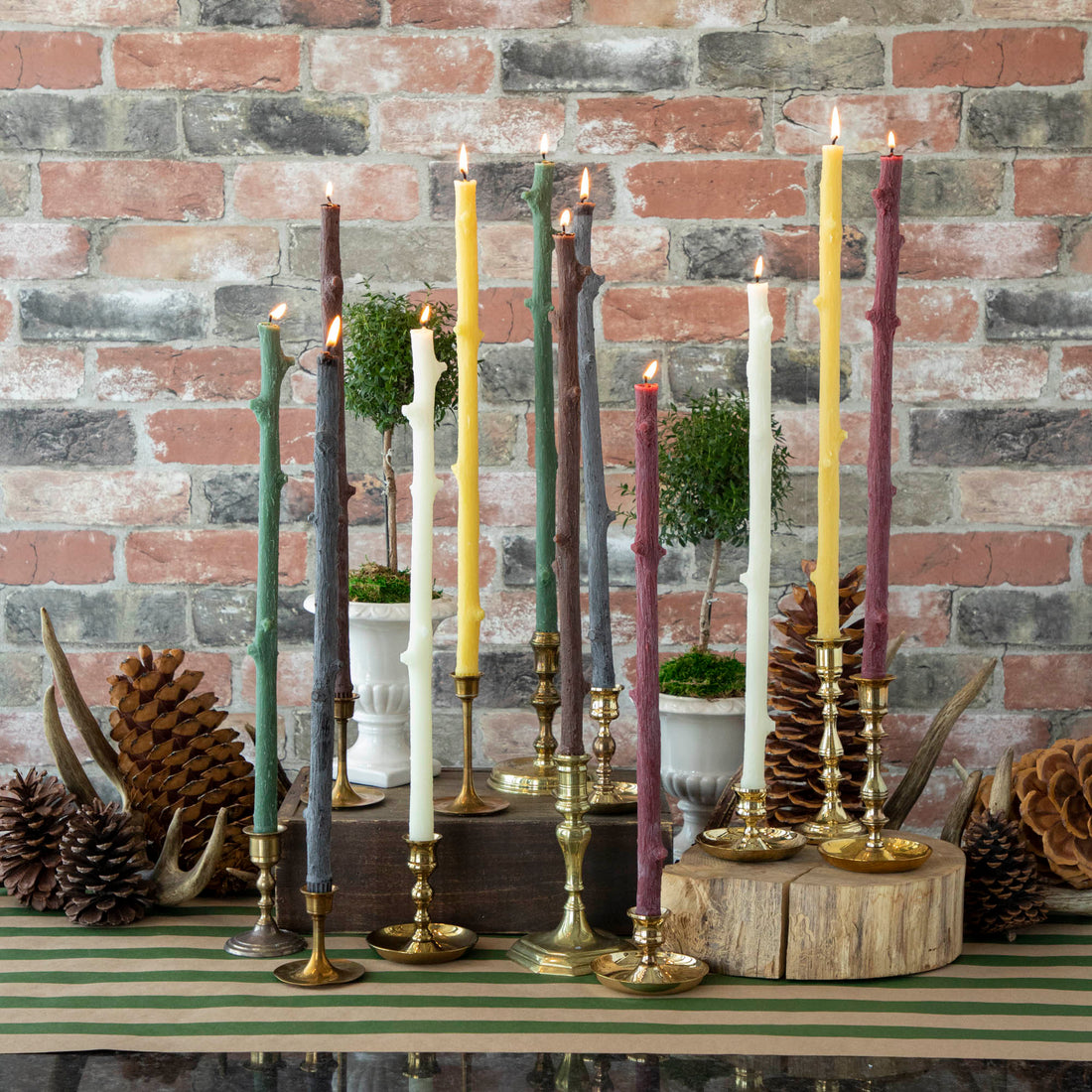 A Stick Candles set and a group of candles on top of a textured brick wall.