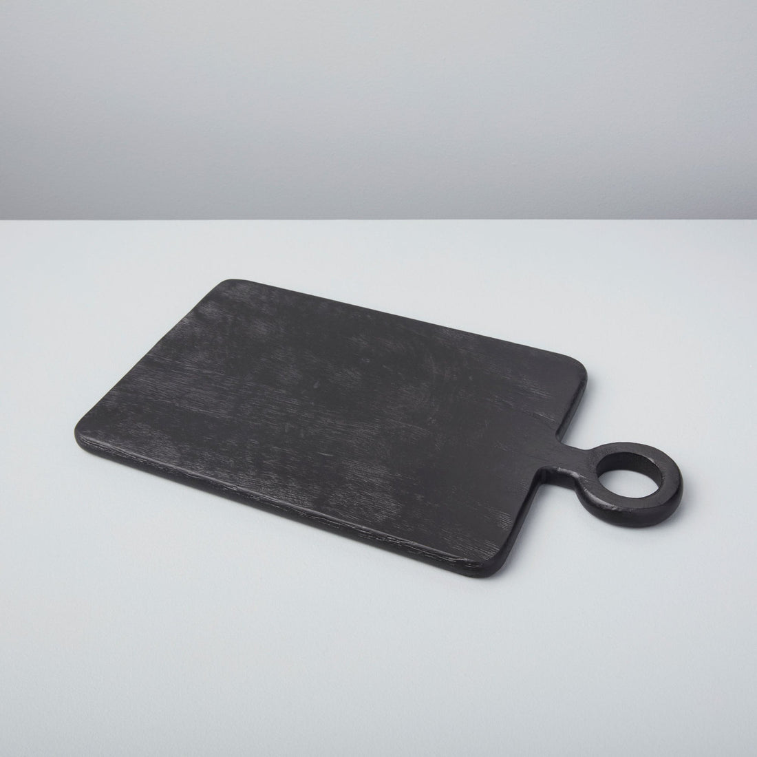 A set of three Be Home Blackened Serving Boards of different shapes and sizes with fresh vegetables displayed in front of a window.