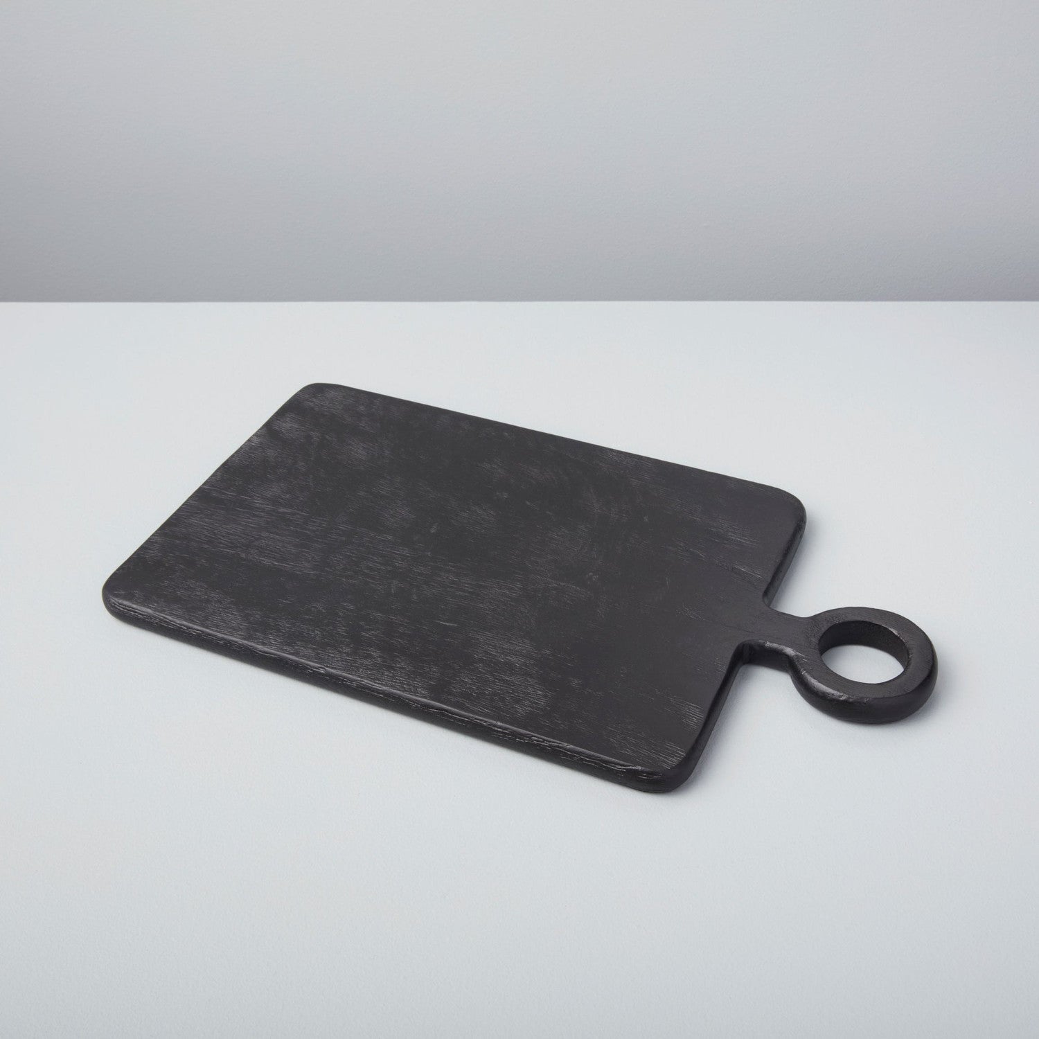 A set of three Be Home Blackened Serving Boards of different shapes and sizes with fresh vegetables displayed in front of a window.
