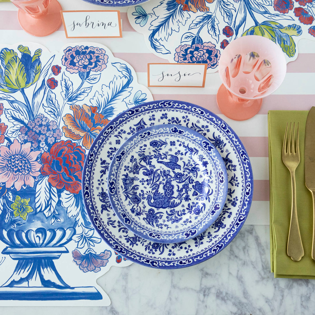 Blue and white patterned Burleigh Blue Regal Peacock Dinnerware plates on a floral patterned background with a name card and a pink glass vase.