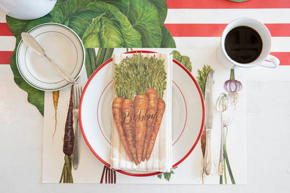 A Carrots Table Accent labeled &quot;Bobby&quot; resting on the plate of a vegetable-themed place setting, from above.