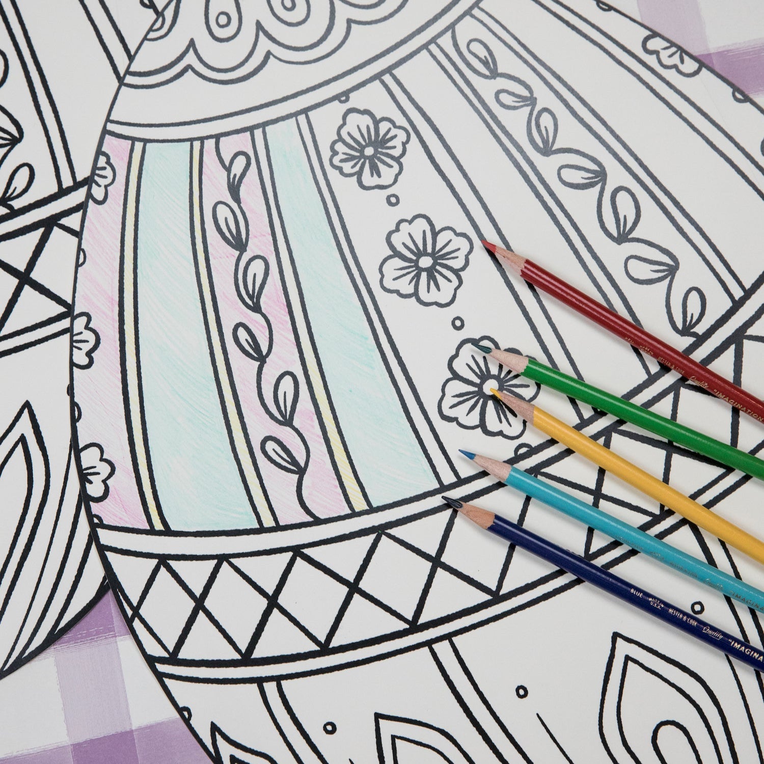The Die-cut Coloring Easter Egg Placemat on an Easter-themed table setting, partially filled in with colored pencils. 
