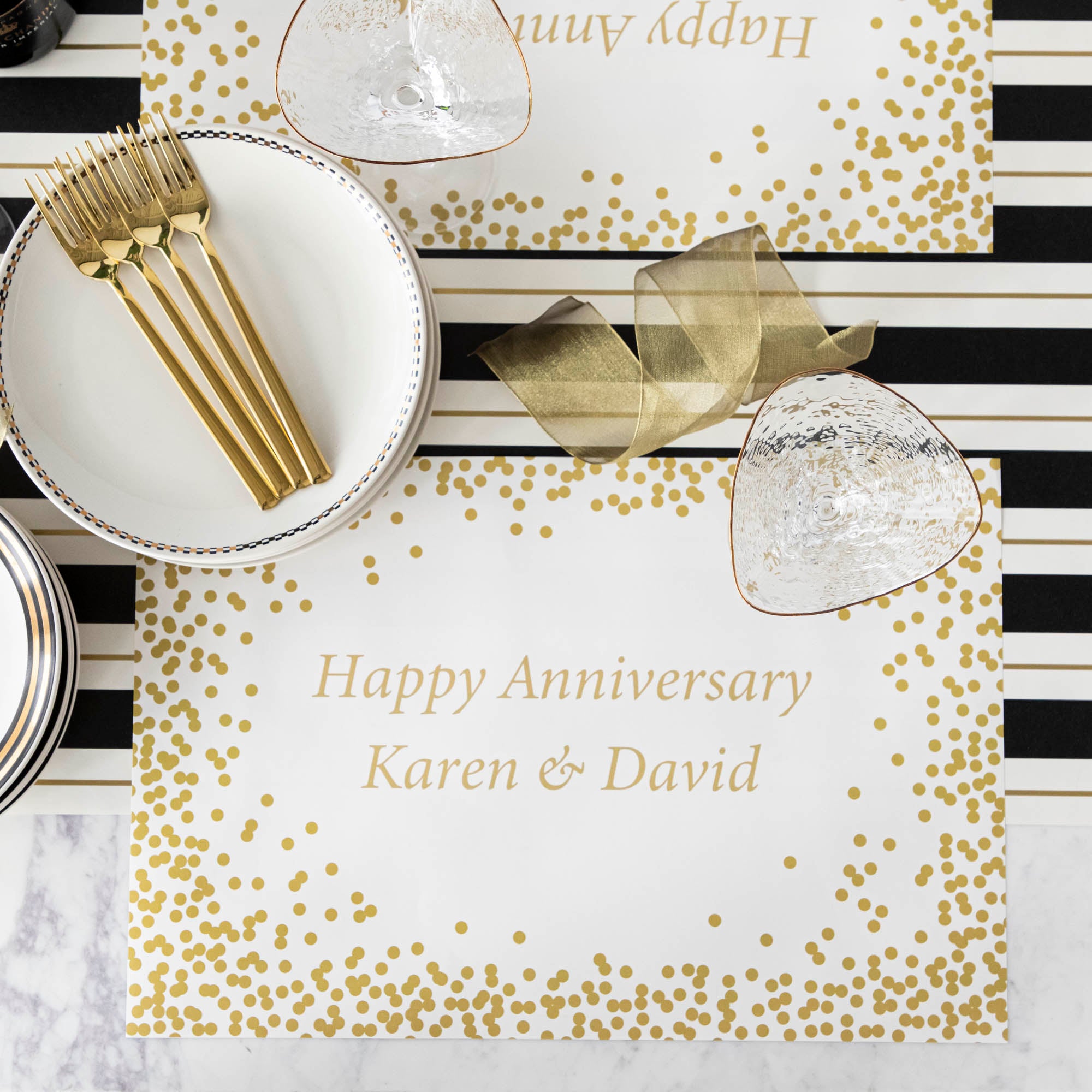 Table setting with Gold Confetti Placemat with personalized message printed in gold color: &quot;Happy Anniversary Karen &amp; David&quot;.