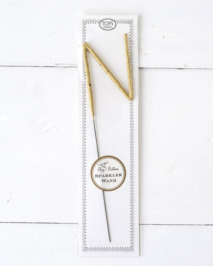 Three Tops Malibu gold Letter Sparklers on a wooden surface.