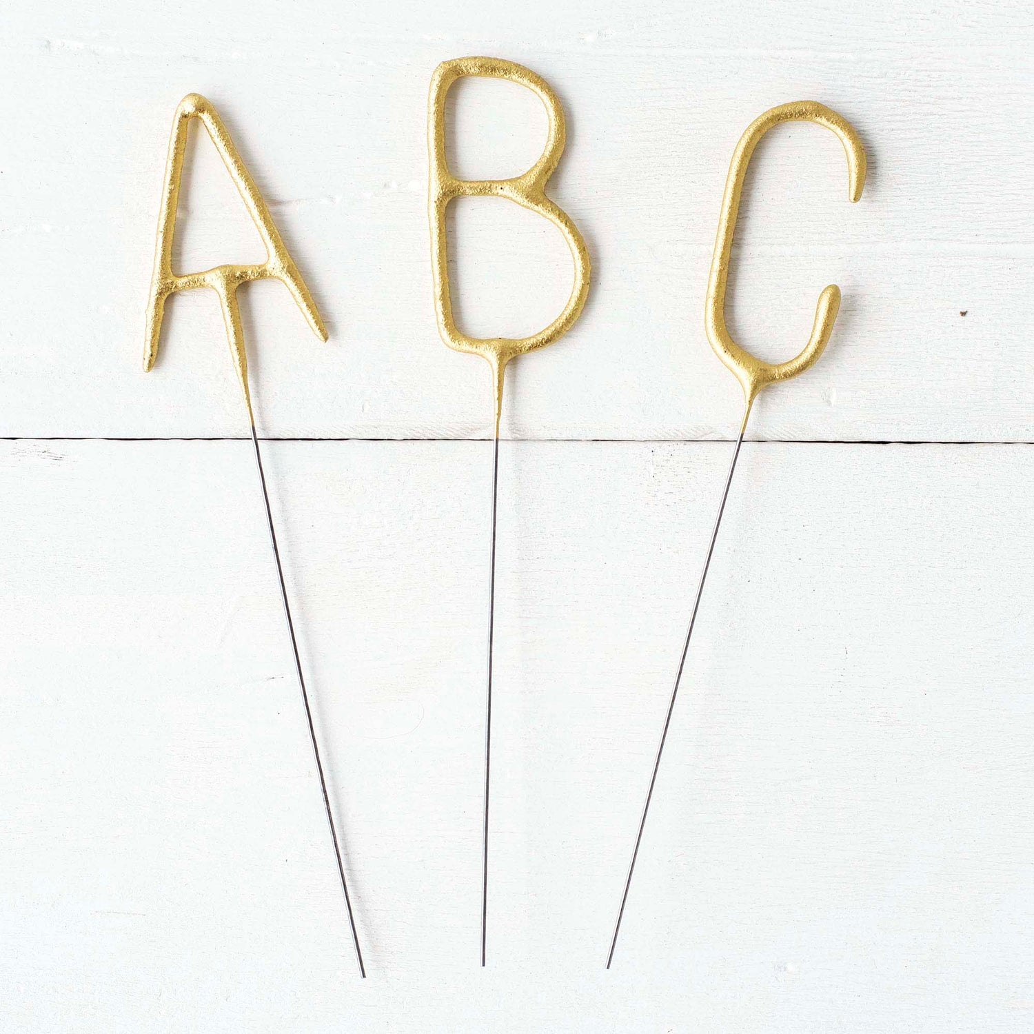 Three Tops Malibu gold Letter Sparklers on a wooden surface.