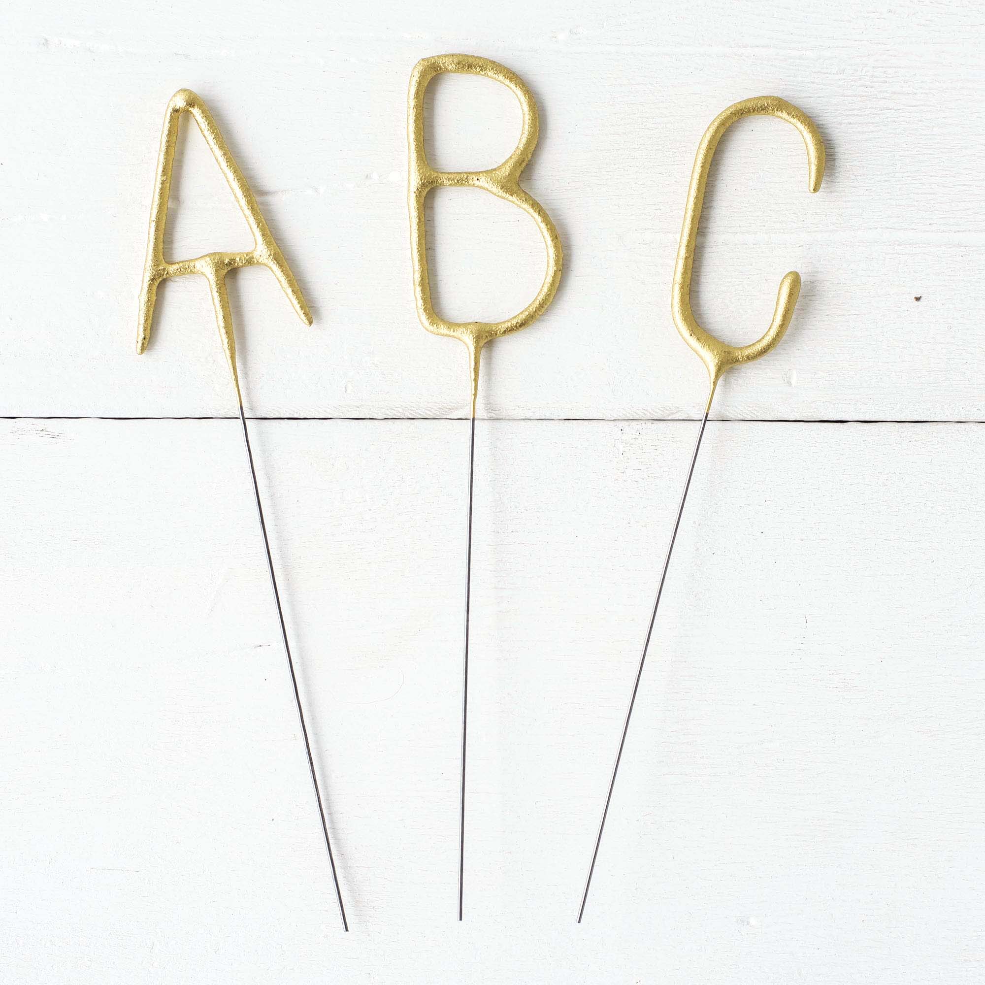 Three Tops Malibu gold Letter Sparklers on a wooden surface.