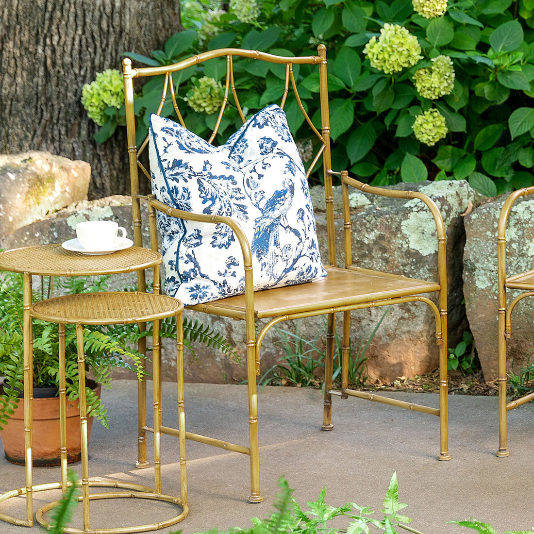A Park Hill metal bamboo porch chair with a blue and white patterned cushion in a garden setting with a matching side table and cup.
