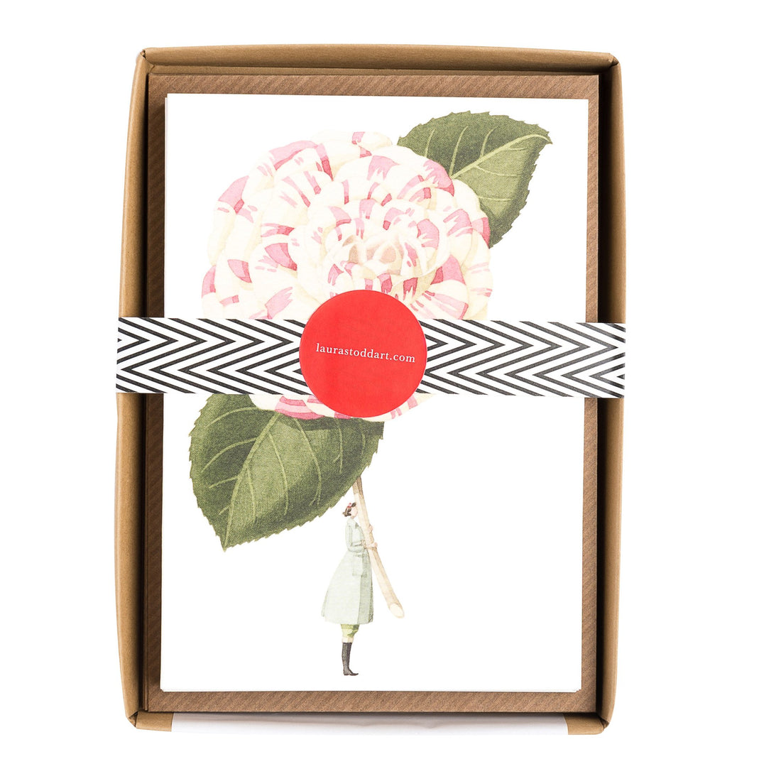 The In Bloom Notecards in retail packaging, showing an illustration of a woman holding a gigantic pink and white flower, with the included kraft envelopes and box wrapped with a belly band. 