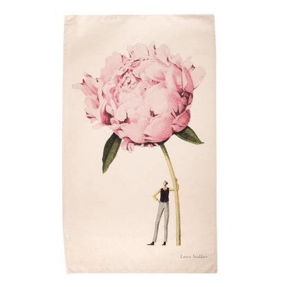 A white tea towel featuring a whimsical illustration of a small man holding a gigantic pink carnation by the stem. Art by Laura Stoddart. 