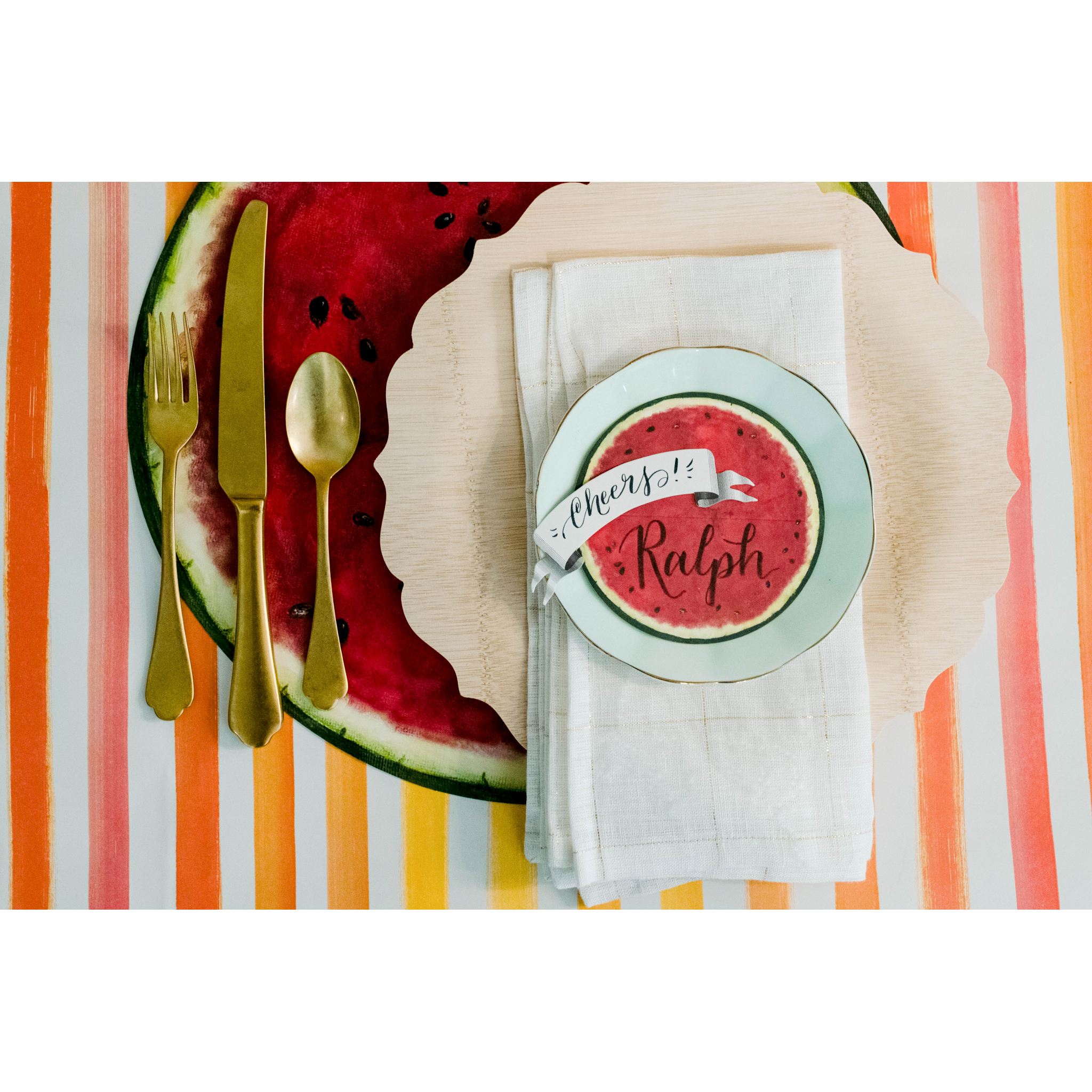 Top-down view of a vibrant summertime place setting, with a Banner Place Card reading &quot;Cheers!&quot; laying flat on the plate.