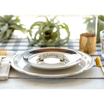 An elegant place setting featuring a Banner Place Card reading &quot;Ginny&quot; standing on the plate.