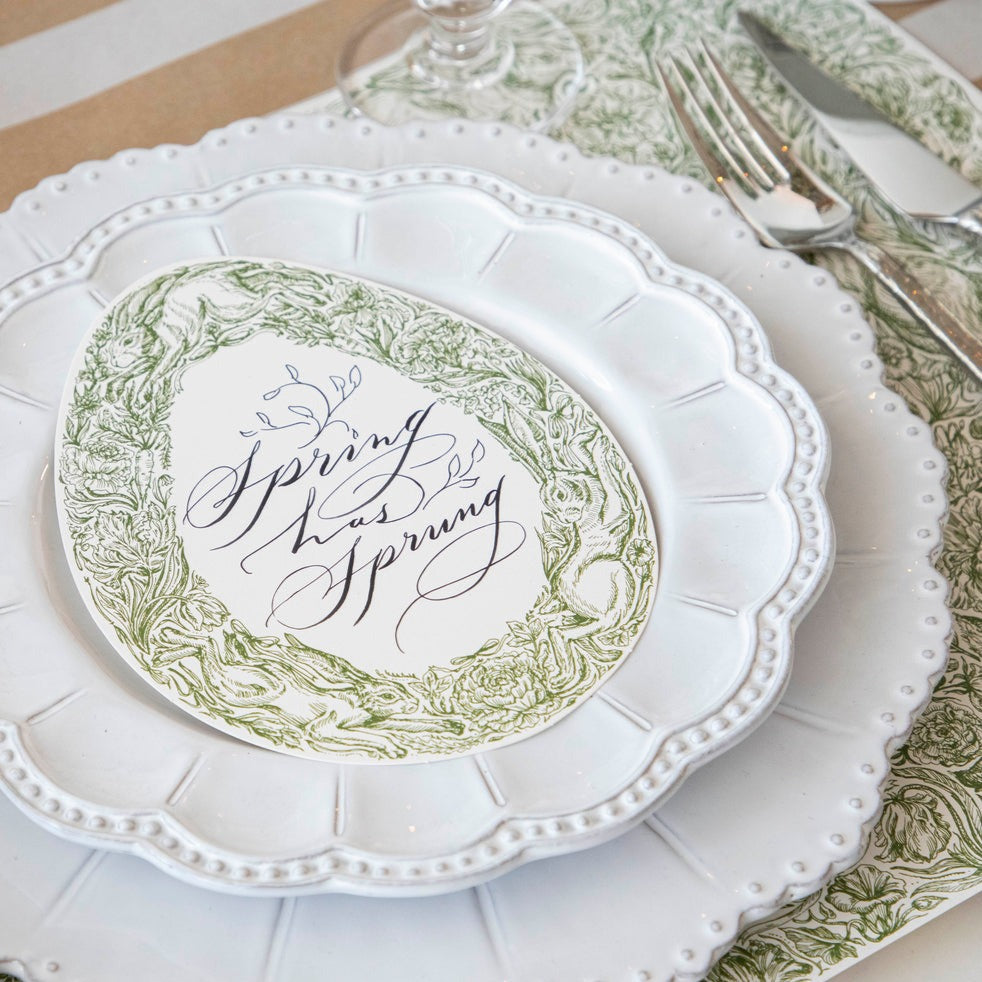 A Greenhouse Hares Table Card with &quot;Spring has Sprung&quot; written on it in elegant script resting on the plate of a Springtime place setting.