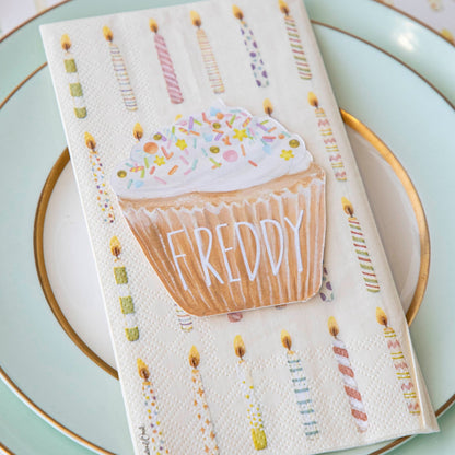 A life-sized Hester &amp; Cook Cupcake Place Card napkin featuring a cupcake and candles, perfect as a party place setting accessory.